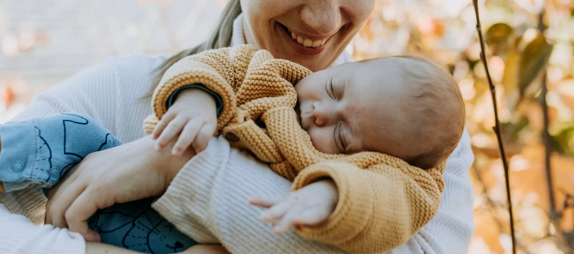 Frau in herbstlicher Umgebung mit Baby auf dem Arm