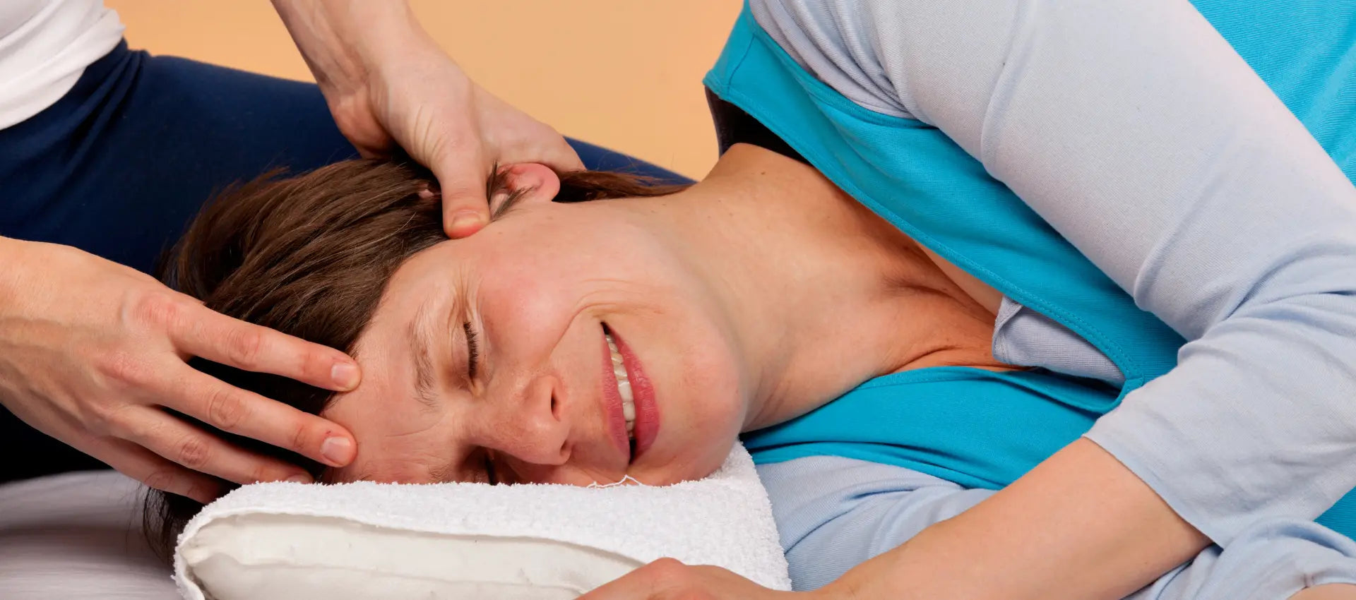 Frau mittleren Alters liegt auf der Seite und erhält eine Druckmassage am Kopf.