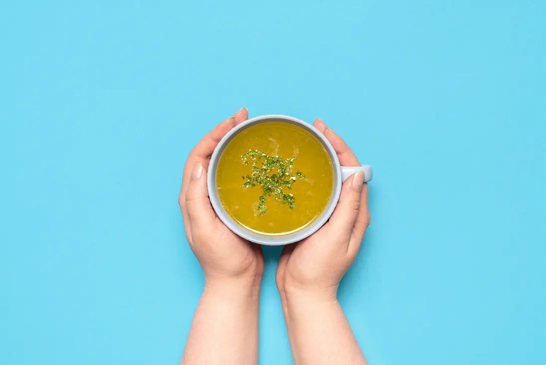 Eine Tasse Suppe von zwei Händen umfasst.