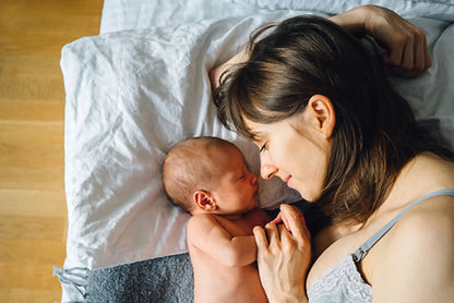 Frau liegt  mit Baby seitlich zueinander im Hintergrund ein Holzboden